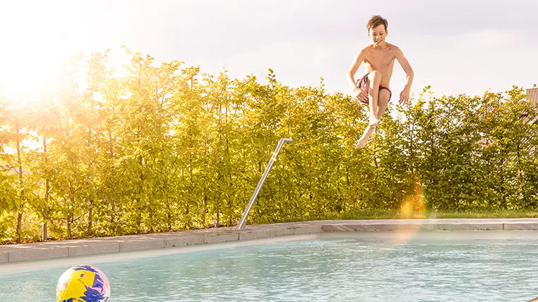 Boy is jumping into a pool on a sunny day