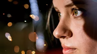 A blonde woman in profile looks seriously into the camera.