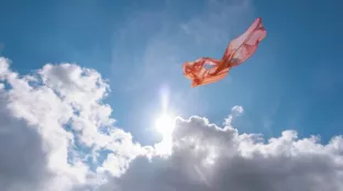 A piece of pink, translucent fabric floating in the sky against bright sunlight and white clouds