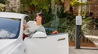 A person enters an electric car with a Fronius Wattpilot Flex charging station visible in the background.